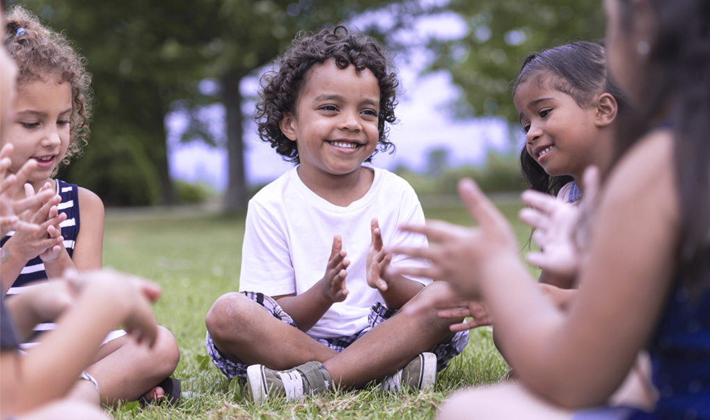 A group of kids sitting on the grass and clapping