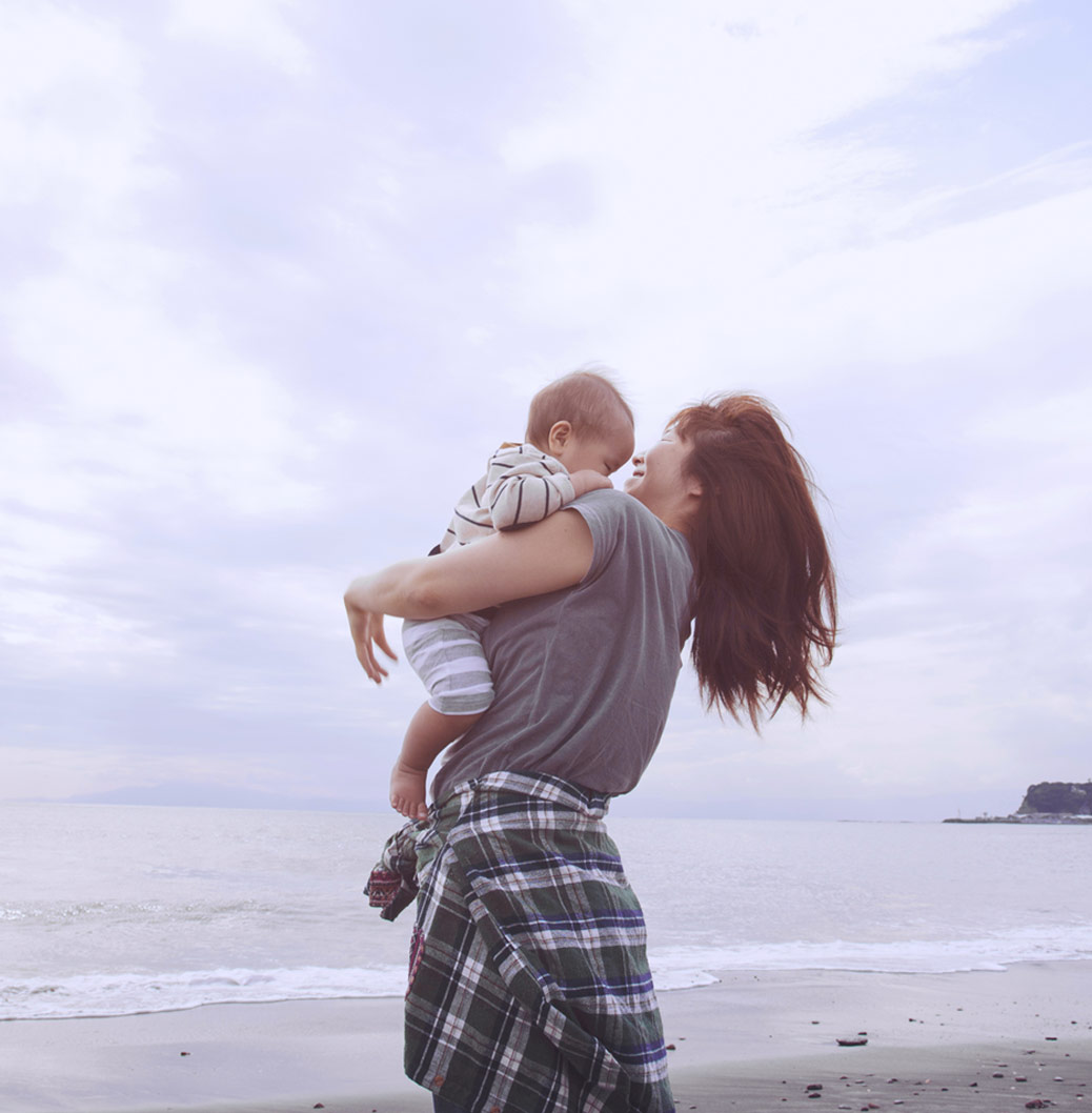 Femme portant un bébé dans ses bras, sur une plage 